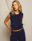 A woman with wavy blonde hair wears the Perfectwhitetee ELLIE terry banded tank and matching loose pants, standing in front of a neutral fabric backdrop with one hand on her hip.