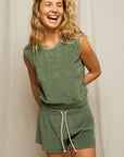 A woman with wavy blonde hair smiles and looks to the side, wearing Perfectwhitetee's Summer Loop Terry Sweat Shorts and a matching sleeveless green top, standing against a plain light-colored background.