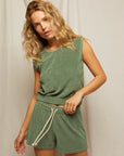 A woman with wavy blonde hair wears Perfectwhitetee's Summer Loop Terry Sweat Shorts and a matching green sleeveless top, standing in front of a plain light-colored fabric backdrop.