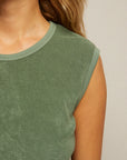 Close-up of a person wearing the ELLIE terry banded tank by Perfectwhitetee in sage green, featuring a ribbed neckline. Their wavy, light brown hair is over one shoulder, with a plain light background and face partially out of frame.
