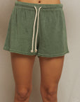A person models Perfectwhitetee's Summer Loop Terry Sweat Shorts in green, featuring a white drawstring and elastic waistband, against a plain light background. Only the torso and upper legs are shown.