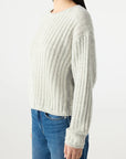 A person, shown from the side against a plain light background, wears the AMO Denim Hallie Sweater in light gray with a ribbed crew neck and long sleeves, paired with blue jeans.