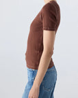 Wearing the AMO Denim Cherish Tee, a ribbed cotton top with a fitted silhouette, paired with light blue jeans and standing in profile against a plain light background.