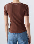 Seen from behind, a person with short hair wears the Cherish Tee by AMO Denim—a ribbed cotton top with a fitted silhouette—paired with blue jeans, set against a plain light background.