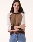 A woman with long brown hair models the BCS Group Nimbus Sweater, a color-block round neck style in brown, tan, and cream, paired with blue jeans and a black belt against a plain light background.
