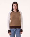A woman with straight brown hair wears the BCS Group Nimbus Sweater—brown with white sleeves and dark brown cuffs—paired with blue jeans, standing against a plain light background.