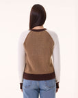 A person with long brown hair, seen from behind, wears the BCS Group Nimbus Sweater—brown with maroon cuffs and collar—paired with blue jeans, standing against a plain light background.