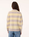 A person with long brown hair, seen from behind, wears the KUJTEN Royde Stripe Sweater with blue jeans against a plain light background.