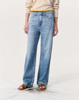 A person models Rag & Bone's Logan Pant in light blue, styled with a beige long-sleeve sweater, brown slide sandals, and a yellow belt against a plain white background. Their head is not visible in the image.
