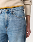 A person wearing Rag & Bone Logan Pant in light blue featherweight denim, styled high-waisted, paired with a cream sweater with yellow trim; shown from waist to mid-thigh.