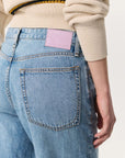 A person is shown from the back wearing Rag & Bone's Logan Pant in light blue Featherweight denim, paired with a cream knit sweater. The focus is on the jeans' back pocket and a pale pink leather patch on the waistband.