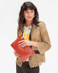 A person with long dark hair holds the vibrant Flat Clutch w/ Tabs by Clare Vivier. They wear a leopard print jacket over a t-shirt with yellow text and black pants, standing against a plain white background.