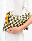 A person in a white button-up shirt holds the Clare Vivier Flat Clutch W/Tabs, a green and cream checkered cotton piece with a yellow fish-shaped keychain on the zipper.
