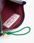 A close-up of the Clare Vivier La Plage Flat Clutch w/tabs shows its red striped lining, a white "Clare Vivier" label, and a green wristlet attached to the gold zipper pull.