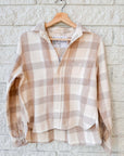 The Silvio Untuckable Shirt by Frank & Eileen, featuring a beige and white plaid pattern and collared design, hangs on a wooden hanger against a light brick wall.