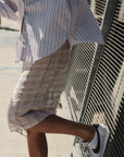 A person in a striped shirt, Cissa Summer Pencil Skirt, and white Nike sneakers leans against a metal fence in bright sunlight.