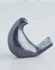 Les Animaux Moineau by Global Views is a small, abstract ceramic bird sculpture with a curved, minimalist design and glossy dark finish, elegantly displayed on a light gray surface.