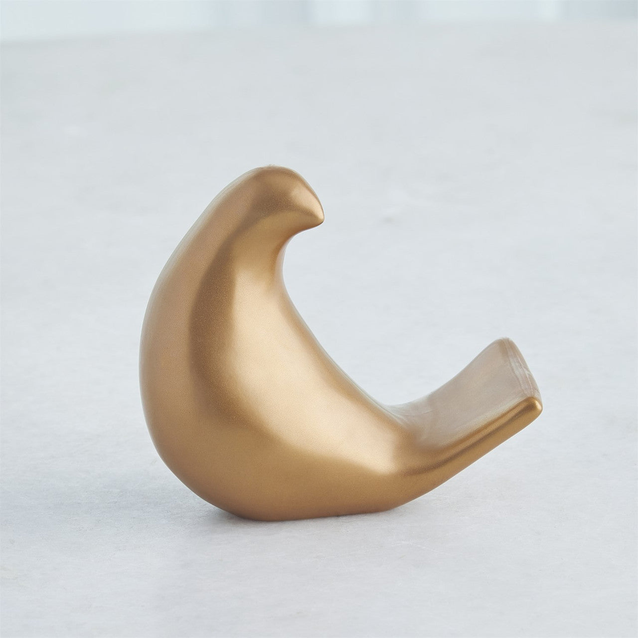The Les Animaux Moineau Gold sculpture by Global Views features a smooth, stylized bird with a rounded body and curved tail in Matte Antique Gold, displayed on a light gray surface.