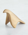 Les Animaux Colombe Gold by Global Views is a smooth, abstract gold sculpture reminiscent of a stylized bird, showcased against a plain, light gray background.