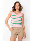 A person with shoulder-length hair wears a sleeveless pink top with green stripes and Kule's beige "The City Short" cotton shorts, made in Italy. They stand against a plain white background with one hand in their pocket.