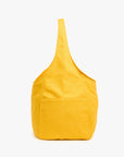 The Clare Vivier Grand Bando Canvas is a bright yellow cotton tote with a wide strap, visible outer stitching, and front pocket, pictured upright against a white background. This vegan bag blends style and practicality.