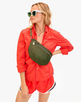 A woman in a bright red button-up shirt and matching athletic shorts poses confidently with white sunglasses, layered necklaces, and carries the Clare Vivier Grande Fanny S25 handwoven leather crossbody bag.