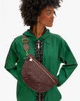 A woman wears a green jacket and a large dark brown Clare Vivier crossbody bag with gold hardware and an Adjustable Crossbody Strap, looking right with hands on hips.