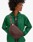 A woman wears a green jacket and a large dark brown Clare Vivier crossbody bag with gold hardware and an Adjustable Crossbody Strap, looking right with hands on hips.