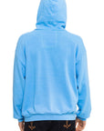 A person is shown from the back wearing the Aviator Nation mountain stitch chevron - pullover hoodie relaxed in bright blue with the hood up, paired with black jeans featuring decorative stitching. The background is plain white.