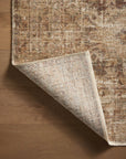 A close-up of a textured Loloi Rugs Bark / Multi Rug with warm, Arizona-inspired tones, partially rolled up to reveal its underside, on a wooden floor.