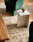 A stylish interior with a modern marble side table holding a small vase of flowers, positioned on a Loloi Rugs Brick / Multi Rug beside a green velvet chair and a wooden table in a Scottsdale Arizona bungalow.