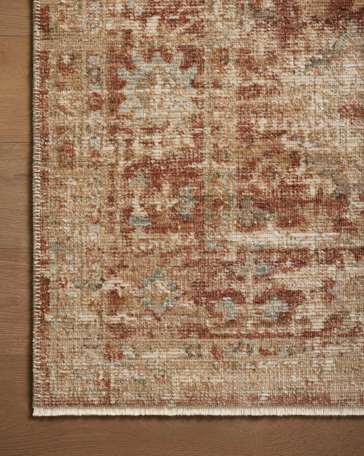 A detailed, ornate Loloi Rugs area rug with a Brick / Multi pattern featuring shades of brown, red, and beige, laid out on the wooden floor of a Scottsdale Arizona bungalow, partially covering it.