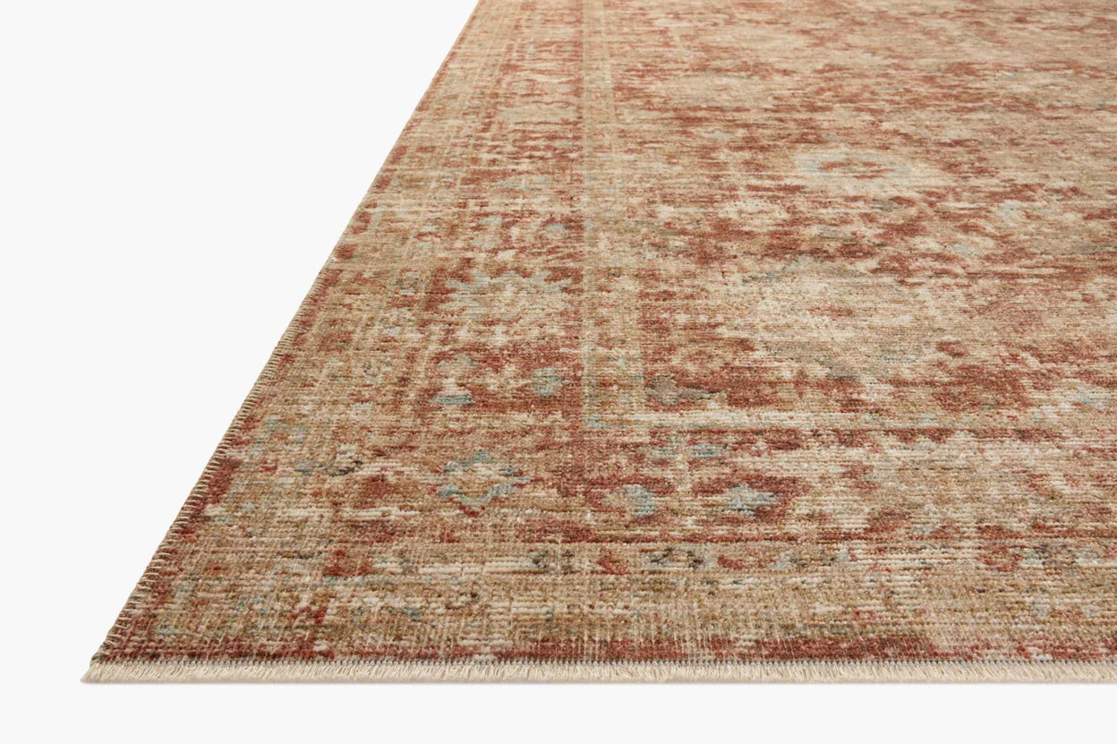 A close-up of a part of a light brown Loloi Rugs Brick / Multi Rug with faded red and blue patterns, on a white background. The edge of the rug is slightly curled in a Scottsdale Arizona bungalow.