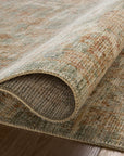 Close-up view of a partially rolled Loloi Rugs Aqua/Terracotta Rug with a faded vintage Arizona-style design in light and dark earth tones on a wooden floor.