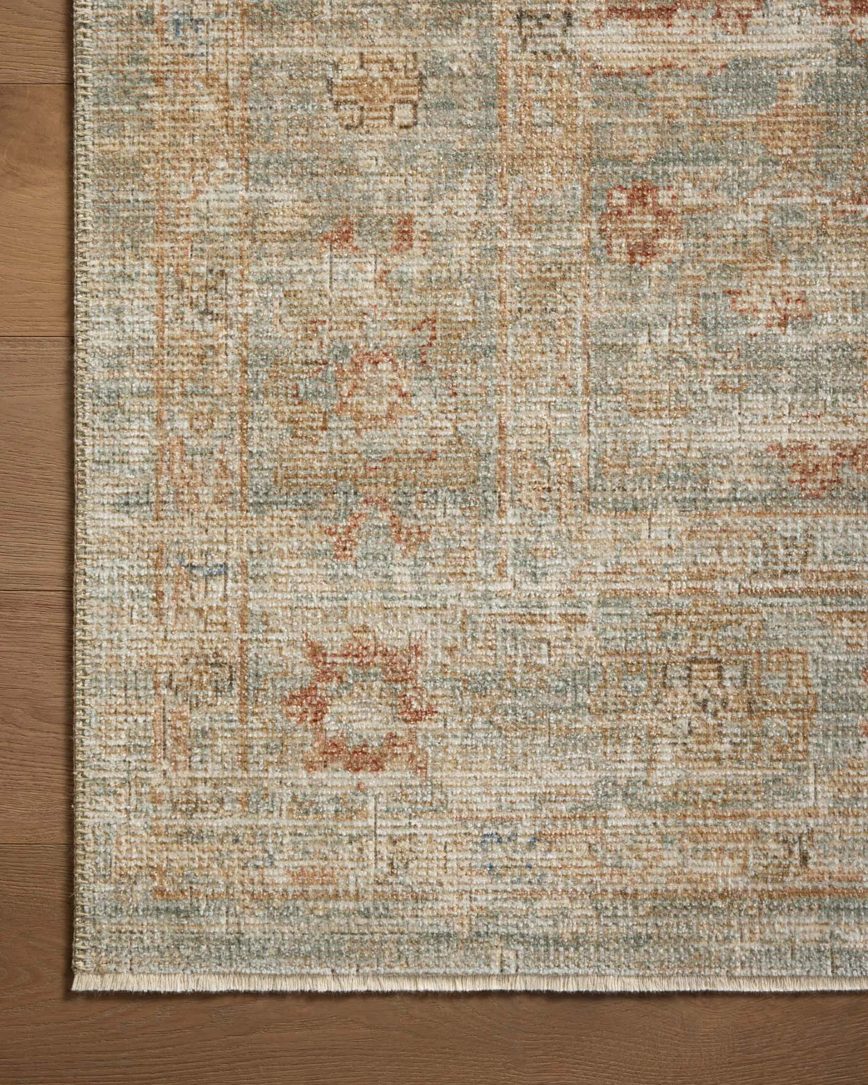 A detailed Loloi Rugs Aqua/ Terracotta Rug with a distressed texture features muted tones of beige and blue, interspersed with subtle red and tan accents, laid on a wooden floor in Arizona style.