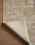 A corner of an Aqua/ Terracotta Rug by Loloi Rugs, with a blend of light and dark hues, primarily gold and faded orange, laid over a wooden floor in Arizona style.