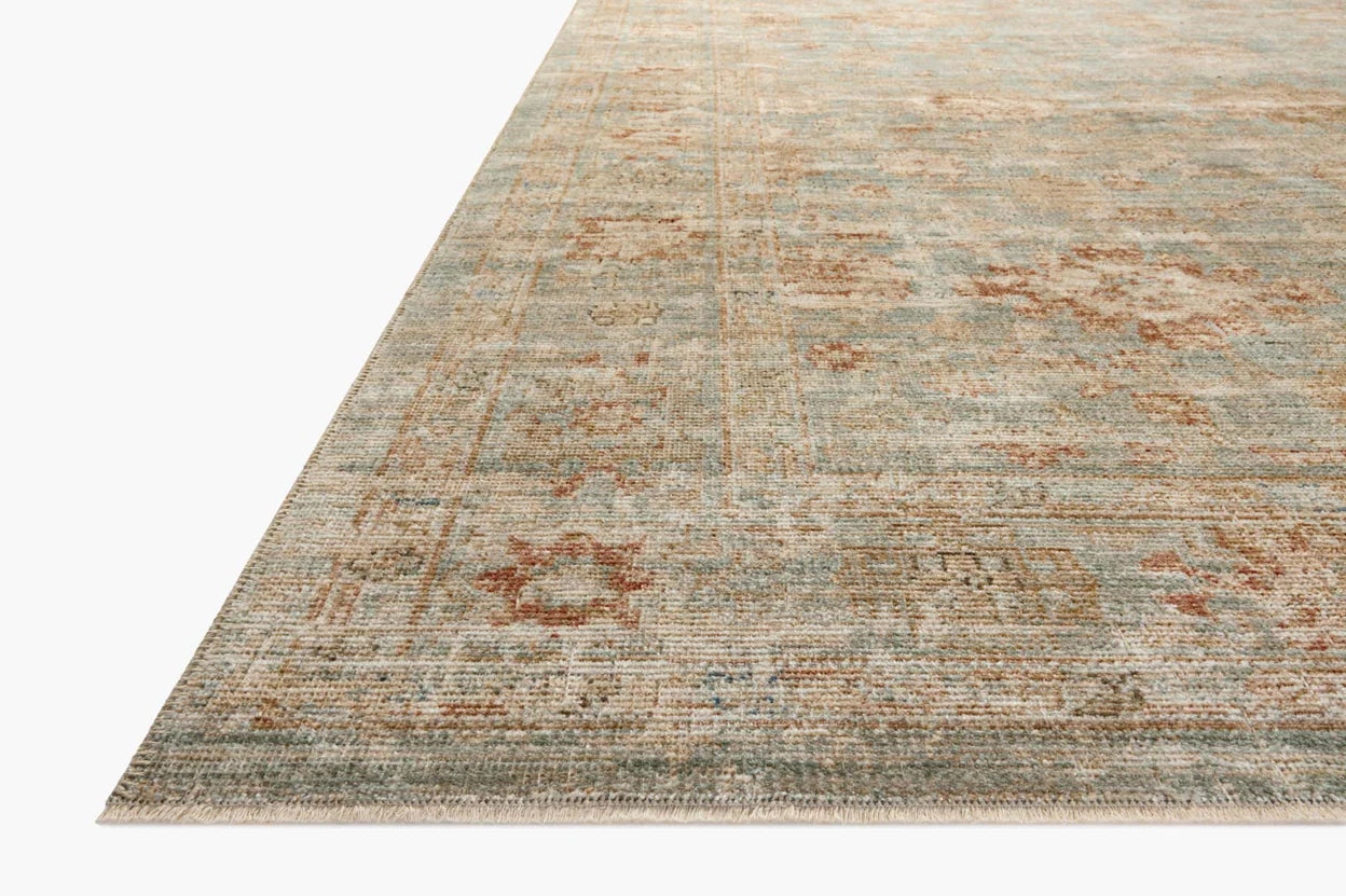 Close-up of a corner of a vintage-style Loloi Rugs Aqua/Terracotta Rug with muted blue and beige tones, displaying a distressed look with subtle floral patterns in a Bungalow style.