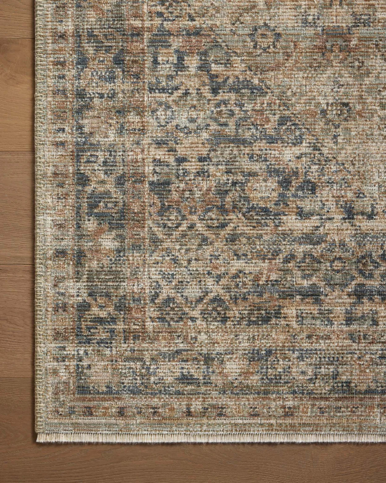 A close-up view of a Sage / Navy Rug by Loloi Rugs with a detailed, vintage-style pattern in muted shades of blues, browns, and creams, displayed on a wooden floor in a Scottsdale Arizona bungalow.