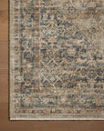 A close-up view of a Sage / Navy Rug by Loloi Rugs with a detailed, vintage-style pattern in muted shades of blues, browns, and creams, displayed on a wooden floor in a Scottsdale Arizona bungalow.