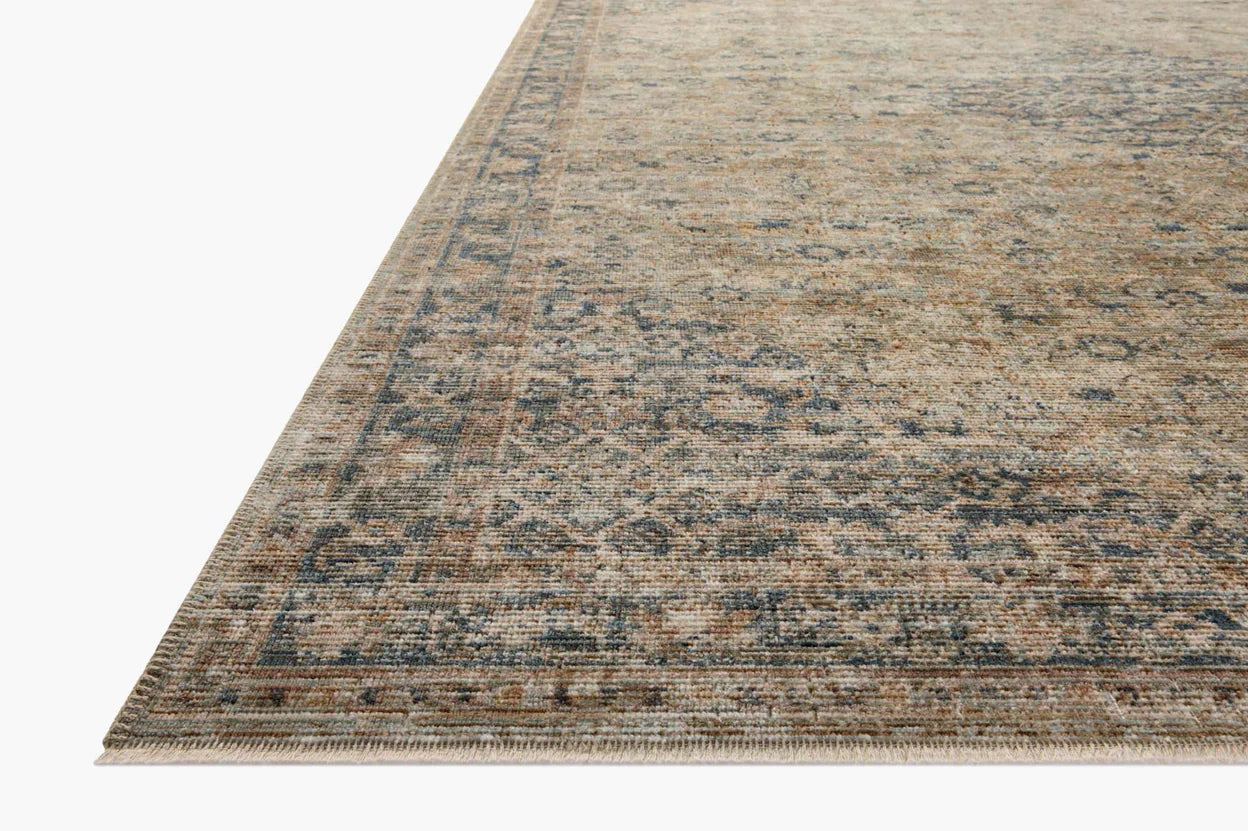 Close-up of a corner of a Sage / Navy Rug by Loloi Rugs with a faded floral pattern in muted beige and blue tones on a white background, evoking the rustic décor found in Scottsdale Arizona bungalows.