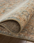 A close-up of a partially rolled-up Ocean / Sand Rug on a wooden floor in a Scottsdale, Arizona bungalow, displaying intricately faded patterns in earth tones from Loloi Rugs.
