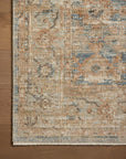 A detailed section of a Ocean / Sand Rug by Loloi Rugs with intricate patterns and a faded color palette of blues, oranges, and beiges, displayed on the wooden floor of a Scottsdale Arizona bungalow.