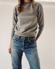 A person wearing The Sweatshirt by Hey Gang and blue jeans stands against a plain white background, with their right hand in their pocket.