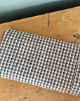 The Modernplum Hertford King Duvet, made from medium weight fabric with a small brown, white, and blue check pattern, is displayed folded on a worn wooden surface.