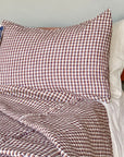 The Hertford King Duvet by Modernplum, featuring brown and white checks, is styled on a neatly made bed with a blue check pillow and nightstand holding a tray of dark stones, set against a light wall.