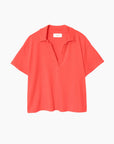 The Spencer Tee by Xirena is a coral red, short-sleeved cotton polo with an open collar and relaxed fit, no buttons, made in Los Angeles and shown against a plain white background.