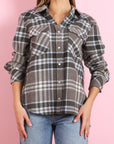 Someone wearing the BCS Group Lumber L/S Shirt—a gray, black, and white plaid 100% cashmere button-up with rolled-up sleeves—and light blue jeans stands against a pink background.