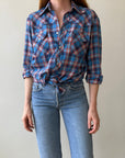A person wears the 1970s Plaid Western shirt by Red Vintage Co., tied at the waist, with loose-fit, ultra-lightweight high-waisted light blue jeans, standing against a plain light-colored background.