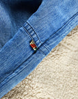 Close-up of the Indigo Sherpa Blanket/Indigo Blues by Free City (sparrow, LLC), showing blue Japanese indigo denim with a multicolored tag near the seam, lying atop soft beige SUPERFLUFF sherpa fleece.