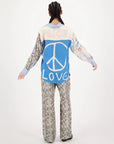 A person with braided hair, seen from behind, wears a colorful shirt with a large blue peace sign and the words "PEACE" above and "LOVE" below, paired with Me369's Bailey Track Pant. The background is plain white.